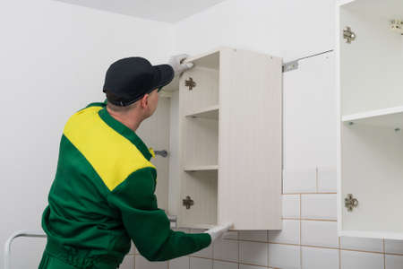 a worker installs a kitchen cabinet on the wall, side viewの写真素材