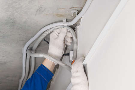 a worker in a helmet lays the cable in the false ceiling, close-upの写真素材