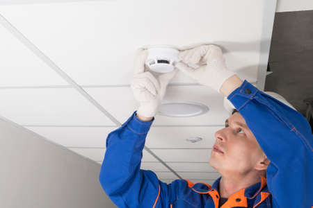 a worker installs a smoke and fire detector on the ceiling in the office, close-upの写真素材