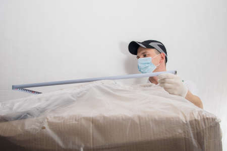 deliveryman measures the dimensions of a large cardboard box with goods with a tape measure, front viewの写真素材