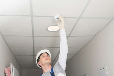 a worker installs a fire safety sensor on a suspended ceilingの写真素材