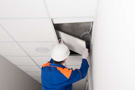 a worker in a helmet dismantles the suspended ceiling, rear viewの写真素材