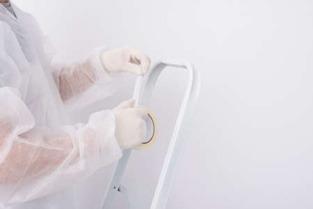 worker holding paper sticky tape while standing on white folding ladderの写真素材