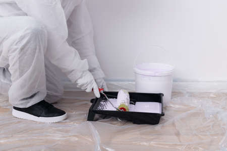 a worker in a protective suit applies paint to a roller, side viewの写真素材