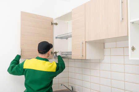 furniture assembly specialist hangs the fronts on the top cabinet of the kitchen unit, rear viewの写真素材