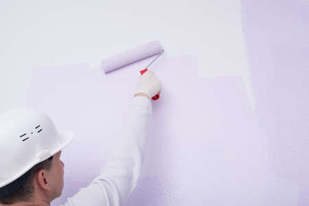a worker in a white uniform, rear view, paints the wallpaper on the wall with a roller, close-upの写真素材