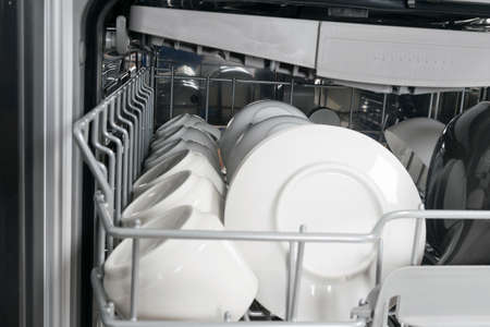 close-up of white saucers and mugs, in the deep compartment of the dishwasherの写真素材