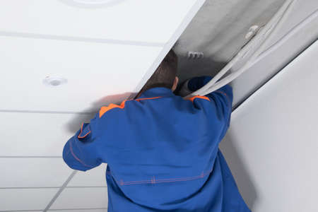 the master repairs hard-to-reach wiring in the suspended ceilingの写真素材