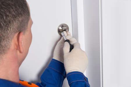 a locksmith in uniform, unscrews the bolt on the front door to close the room from the insideの写真素材
