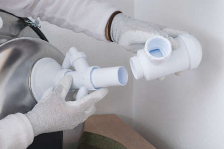 a specialist in protective gloves, collects and installs a white sewer pipe on a metal sinkの写真素材