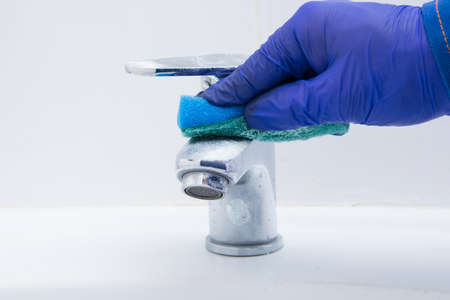 cleaner's hand, cleaning the dirty faucet, sponge with detergent, in the bathroomの写真素材