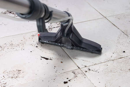 on the white tile floor, a washing vacuum cleaner removes dirty shoe marks after the street, close-upの写真素材