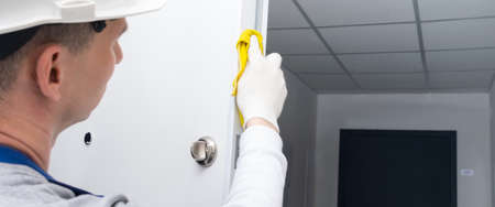 after oiling the door mechanism, the master in protective gloves and a hard hat, wipes the edges of the doors and locks with a yellow clothの写真素材