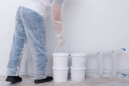 a man in protective clothing, bringing buckets of paint and a set of tools, against a white wallの写真素材