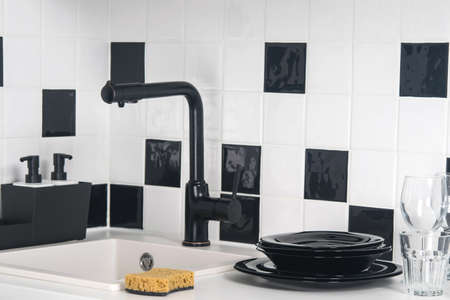 on the table, against the background of black and white tiles, there is a stack of dishes, cleaning agent, there is a sink with a tapの写真素材