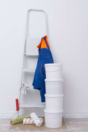 against a white wall, building materials, paint buckets, rollers, a stepladder and protective clothingの写真素材