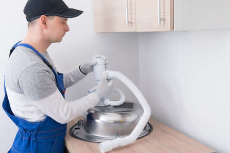 a specialist in protective clothing and gloves, collects and installs a white sewer pipe on a metal sinkの写真素材