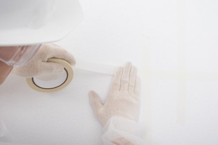 a worker glues an adhesive tape to the joint between a wall and a ceiling, close-upの写真素材