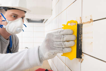master rubbing the seams on the laid white tiles on the wall, finishing workの写真素材