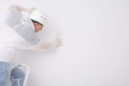 Worker pastes white wallpaper on the wall, on the right is a place for your inscriptionの写真素材