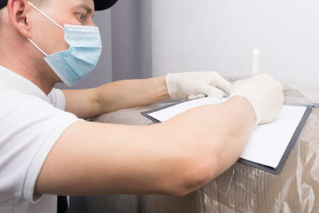 a courier in a mask fills out documents for delivered goods from an online store, close-upの写真素材