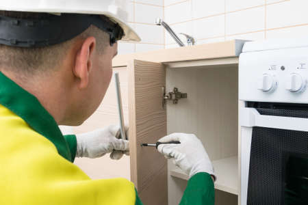 a worker installs the handle on the door of the lower cabinet of kitchen furniture with a screwdriver, professional furniture assemblyの写真素材