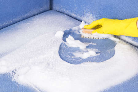 hand in a rubber glove dry-cleaning upholstered furniture with a brush, close-upの写真素材