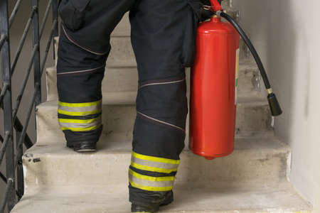 a firefighter climbs the stairs and carries a red fire extinguisherの写真素材