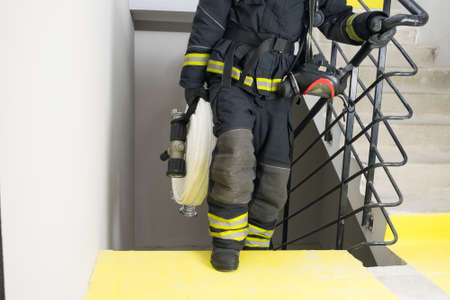 a firefighter climbs the stairs and carries a hose line and equipment for extinguishing fires indoors, front viewの写真素材