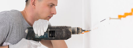 a worker works with a puncher, makes holes in the wall, long photoの写真素材
