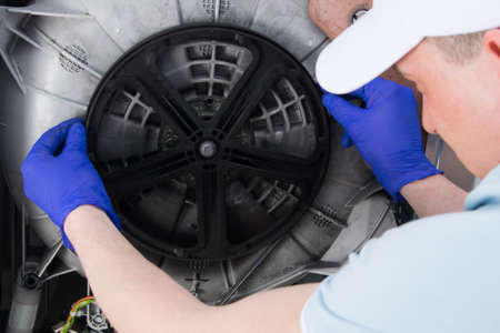 the master in protective form puts on the belt of the drive of the washing machine, drum, close-upの写真素材