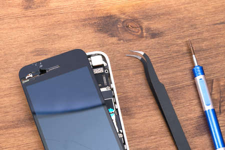 on a wooden table, a phone with a removed liquid crystal screen to replace it, a screwdriver and tweezersの写真素材