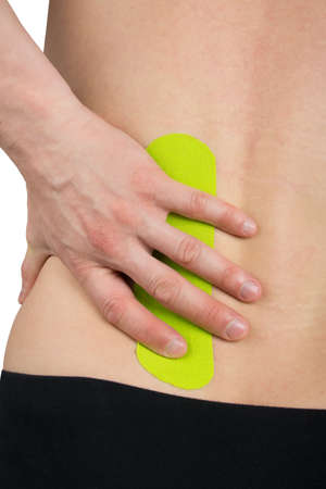 the hand holds the back of the back with a taped tape to relieve lower back pain, after an injuryの写真素材