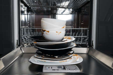 dirty white and black plates, standing in front of an open dishwasherの写真素材