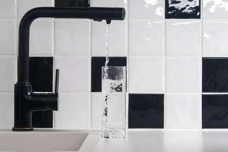 tap water is poured into a transparent glass, against a background of black and white tilesの写真素材