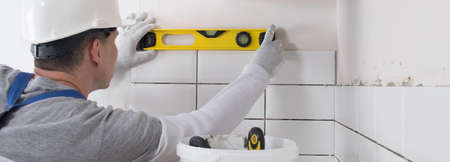 The senior master accepts the correct laying of tiles on the wall using the yellow level, close-upの写真素材