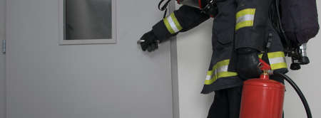a firefighter in protective clothing and with a fire extinguisher opens the iron doorの写真素材