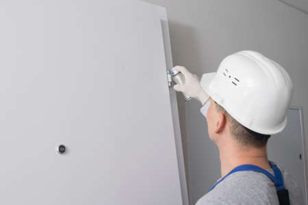 a man in a work uniform, smears the hinges of the front door, with grease from a cylinderの写真素材