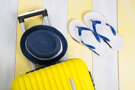 on a light wooden striped background there is a yellow suitcase and a set of things for recreation a hat shoes flip flopsの写真素材