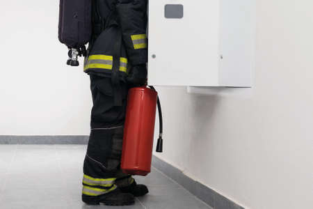 a firefighter with a fire extinguisher is looking for a short circuit and a fire in the electrical...