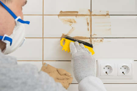 master rubbing the seams on the laid white tiles on the wall, finishing work, back viewの写真素材
