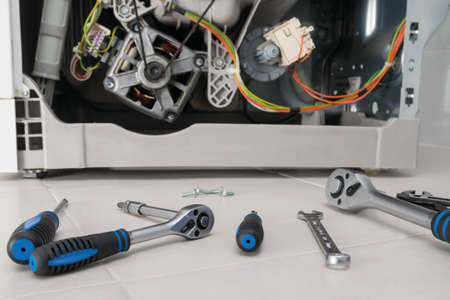 tools for repairing the washing machine are laid out in front of the washing machine mechanismの写真素材