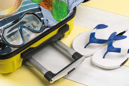 set of things for a beach vacation in an open yellow suitcase, side viewの写真素材
