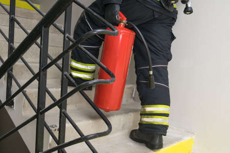 a firefighter climbs the stairs and carries a red fire extinguisher to extinguish fires in electrical equipmentの写真素材