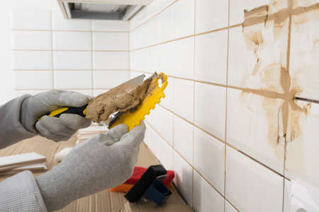 the hands of the master apply brown grout to the spatula, finishing work in the apartmentの写真素材
