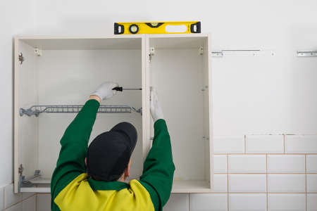 furniture assembler assembles the top cabinets of a kitchen set, rear viewの写真素材