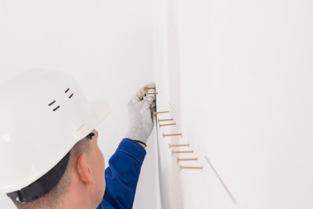 a worker in a helmet inserts self-tapping screws into pre-made holes in a white wall, side viewの写真素材
