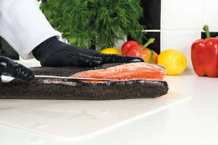 chef cuts raw trout on a white board. Ingredients for the dish lemon, red pepper, green saladの写真素材