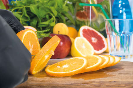 the chef in the kitchen prepares lemonade from fresh fruits, cuts an orange. Ingredients lemon, mint, apples.の写真素材