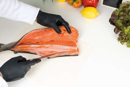 chef cuts raw trout on a white board, top view. Ingredients for the dish lemon, red pepper, green saladの写真素材